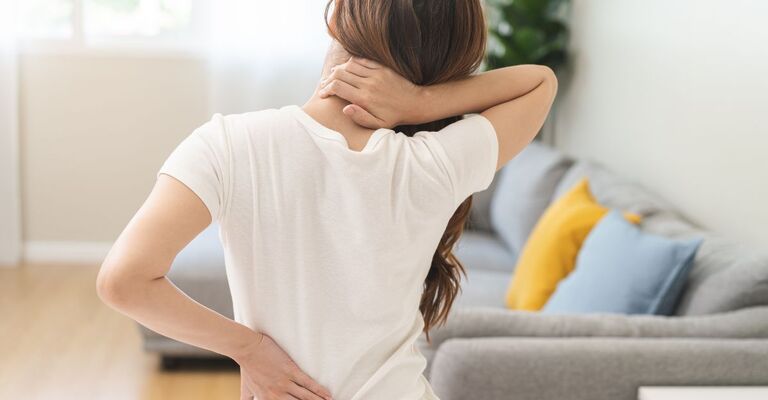 donna si mette una mano sulla schiena dolorante