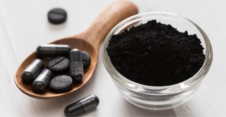 Carbone vegetale nero in una ciotola e sotto forma di compresse
