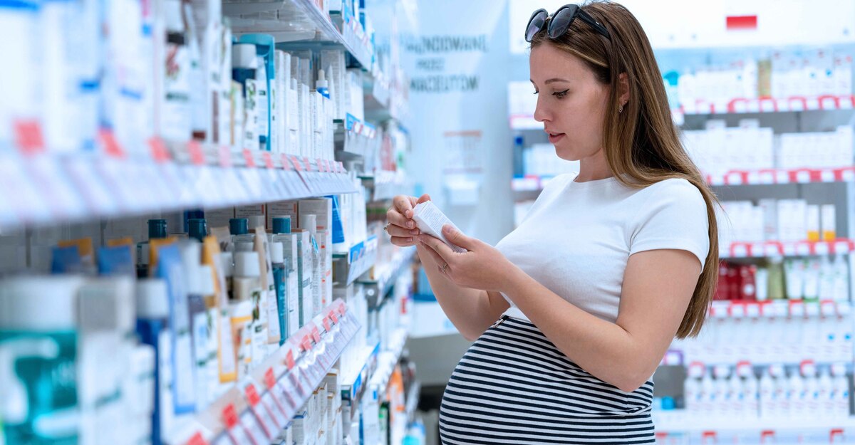 Una donna incinta in farmacia guarda una medicina tra gli scaffali