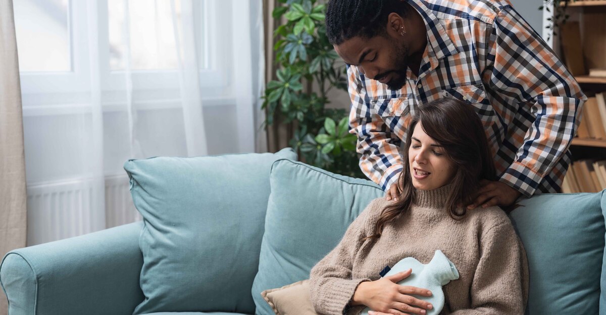 Marito accudisce la moglie sofferente sul divano con borsa dell'acqua calda