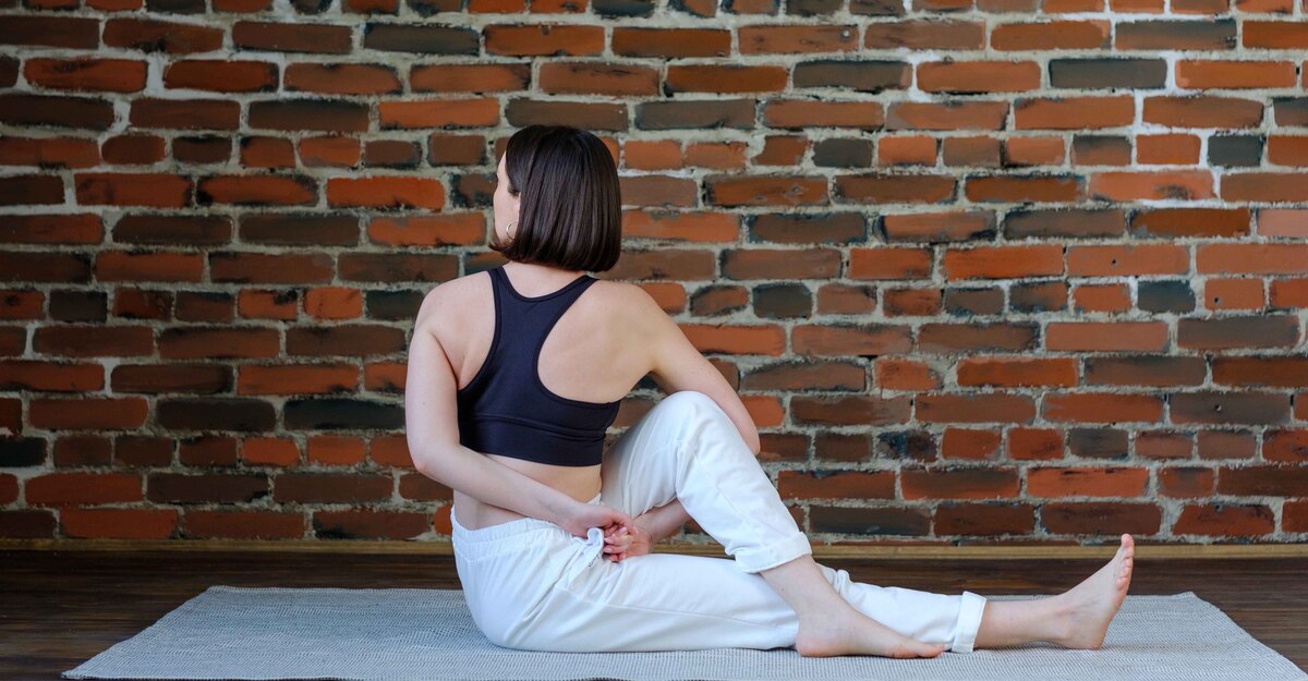 Una donna seduta su un tappetino esegue un esercizio di stretching per dorsali