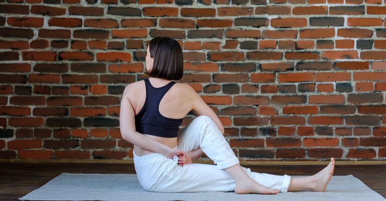 Una donna seduta su un tappetino esegue un esercizio di stretching per dorsali