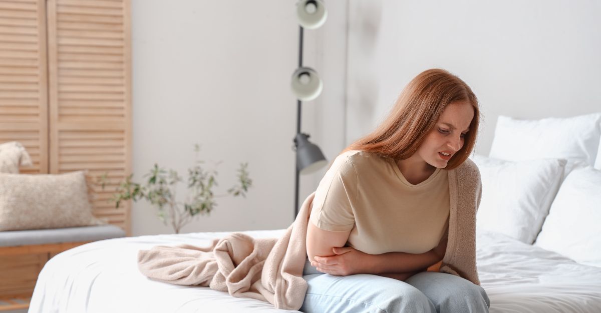 Ragazza seduta sul letto si tiene l'addome per i dolori mestruali