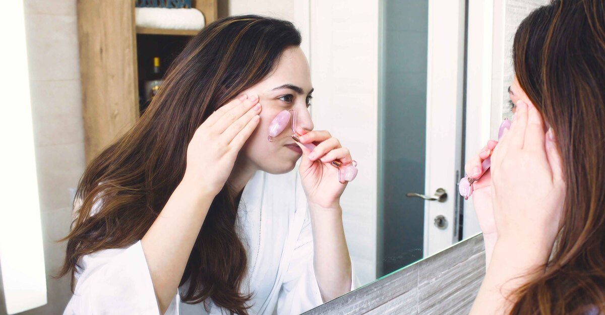 Una ragazza applica il rullo di giada sul viso allo specchio