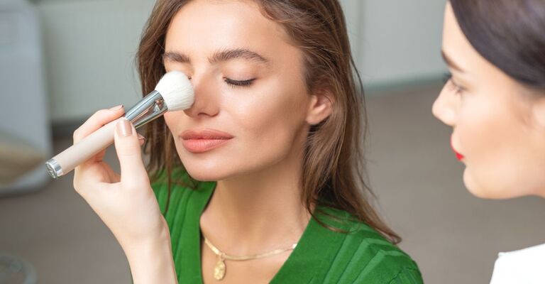 Una truccatrice trucca il naso di una donna