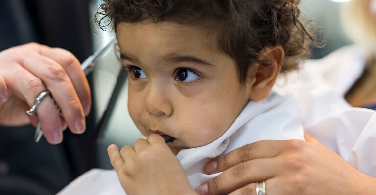 Bambino sostenuto mentre gli vengono spuntati i capelli