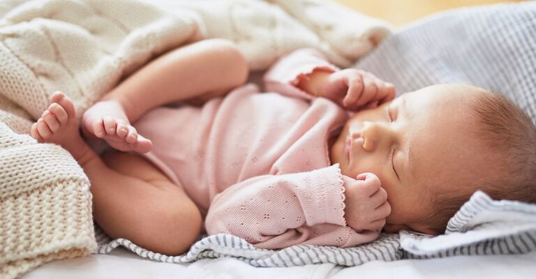 Neonato sdraiato che dorme con le mani appoggiate sulle guance