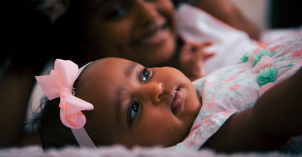 Bambina sdraiata in primo piano e la sua mamma che sorride in secondo piano