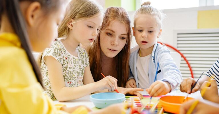 Donna con bambine che giocano sul tavolo con pittura e colori