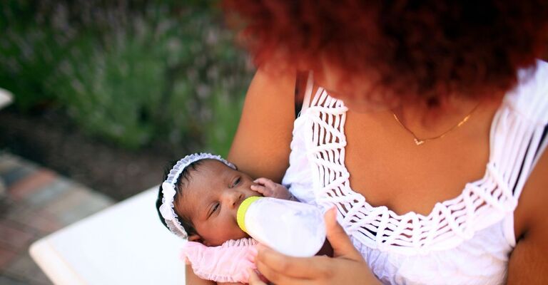 Donna allatta neonata fuori casa con biberon