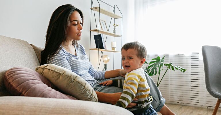 mamma seduta sul divano con bambino che fa i capricci