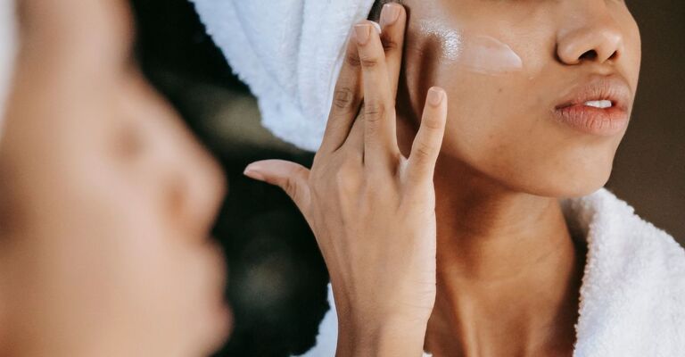 Una ragazza si applica della crema sul viso mentre è allo specchio