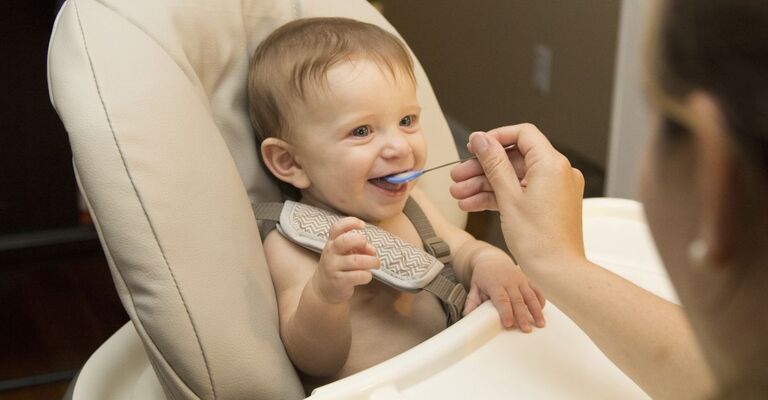 Neonato sorridente mangia imboccato sul seggiolone