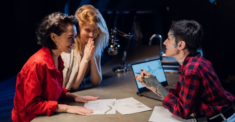 Due amiche parlano con una tatuatrice del tatuaggio che vogliono fare