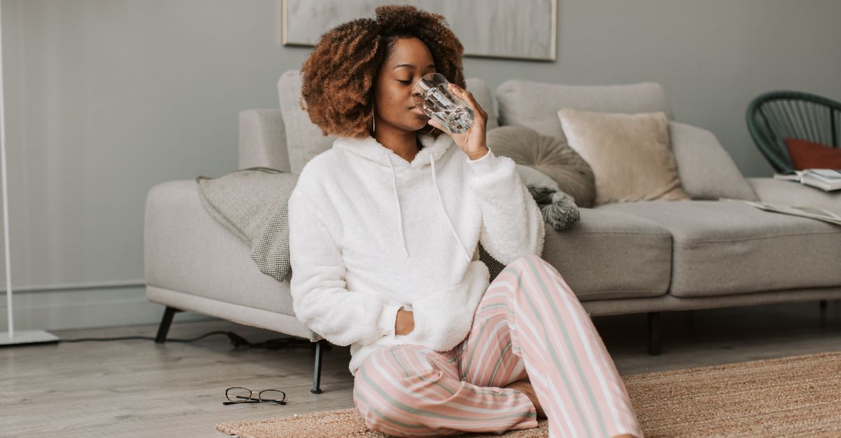 Donna seduta in salotto beve un bicchiere d'acqua