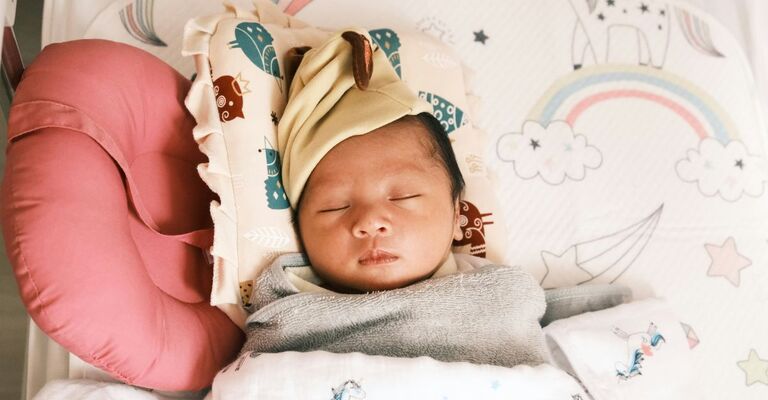 Neonata su un lettino circondata da cuscini 