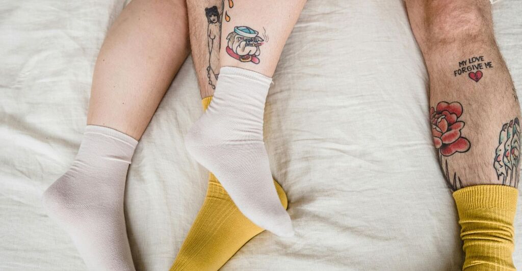 Due gambe tatuate di una coppia sdraiata sul letto