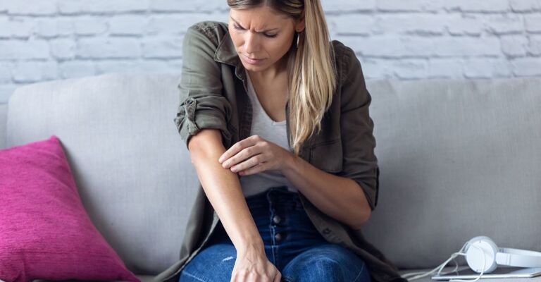 ragazza seduta sul divano si gratta il braccio