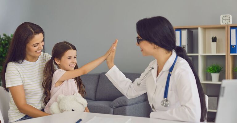 Una bambina da il cinque ad una dottoressa mentre è in braccio alla madre