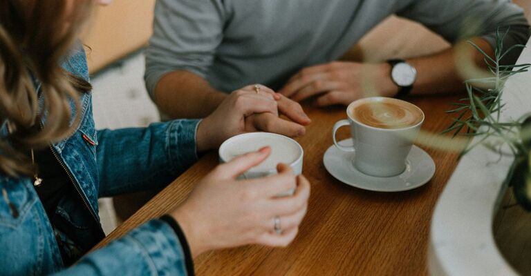 Due persone sedute al bancone che prendono un cappuccino mano nella mano