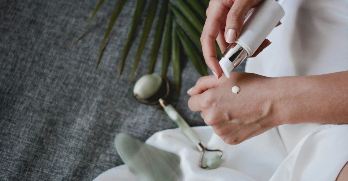 Mano con crema viso sul dorso e alcuni strumenti per la skincare sullo sfondo