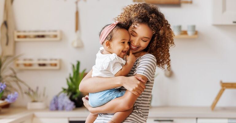 Neonata che ride in braccio alla mamma che la avvolge e ride con lei
