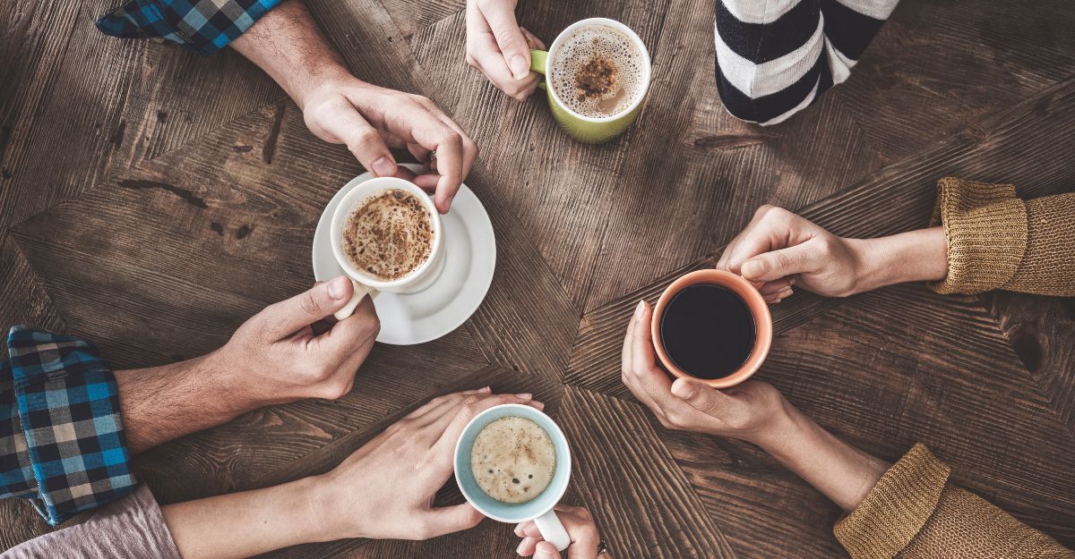 Gruppo di mani con tazze in mano poggiate su un tavolo di legno