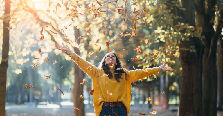 ragazza al parco lancia in aria le foglie secche
