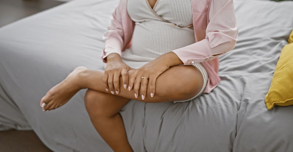 Donna incinta seduta sul letto che si tiene una gamba