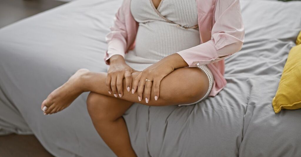 Donna incinta seduta sul letto che si tiene una gamba