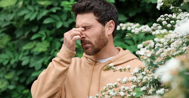 ragazzo sta per starnutire vicino ad un albero in fiore