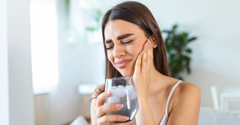 ragazza ha un bicchiere di acqua in mano e sente dolore alla bocca
