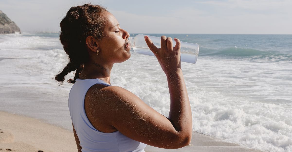 Ragazza beve acqua in spiaggia dalla boraccia