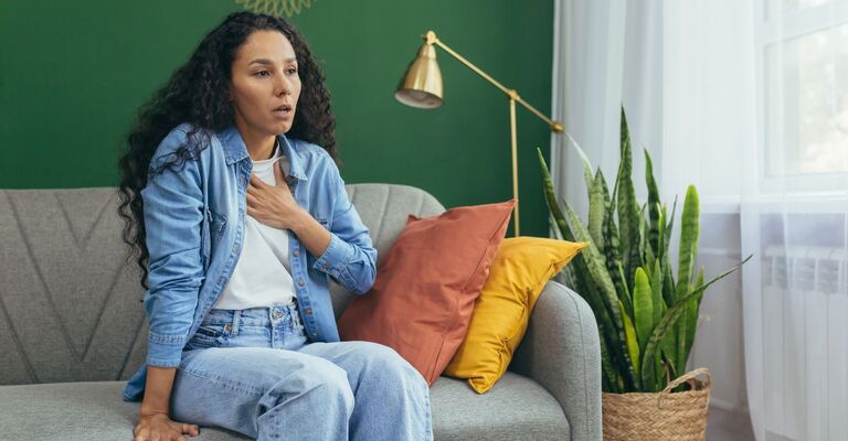 Donna con la mano sul petto mentre è seduta sul divano