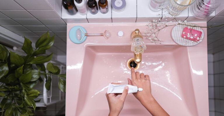 Mano che applica prodotto sulla mano davanti a un lavandino