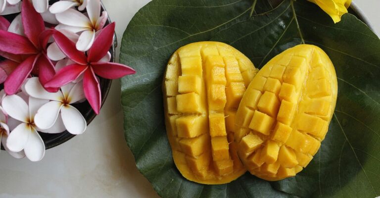 Mango tagliato su una foglia e vicino a dei fiori