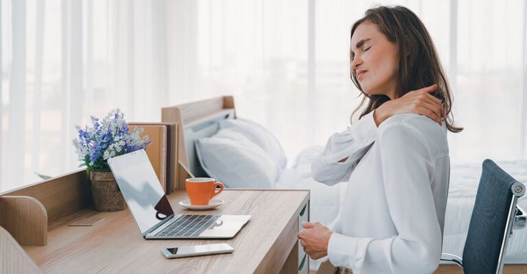 Ragazza seduta alla scrivania che lavora al PC che si tocca il collo dolorante