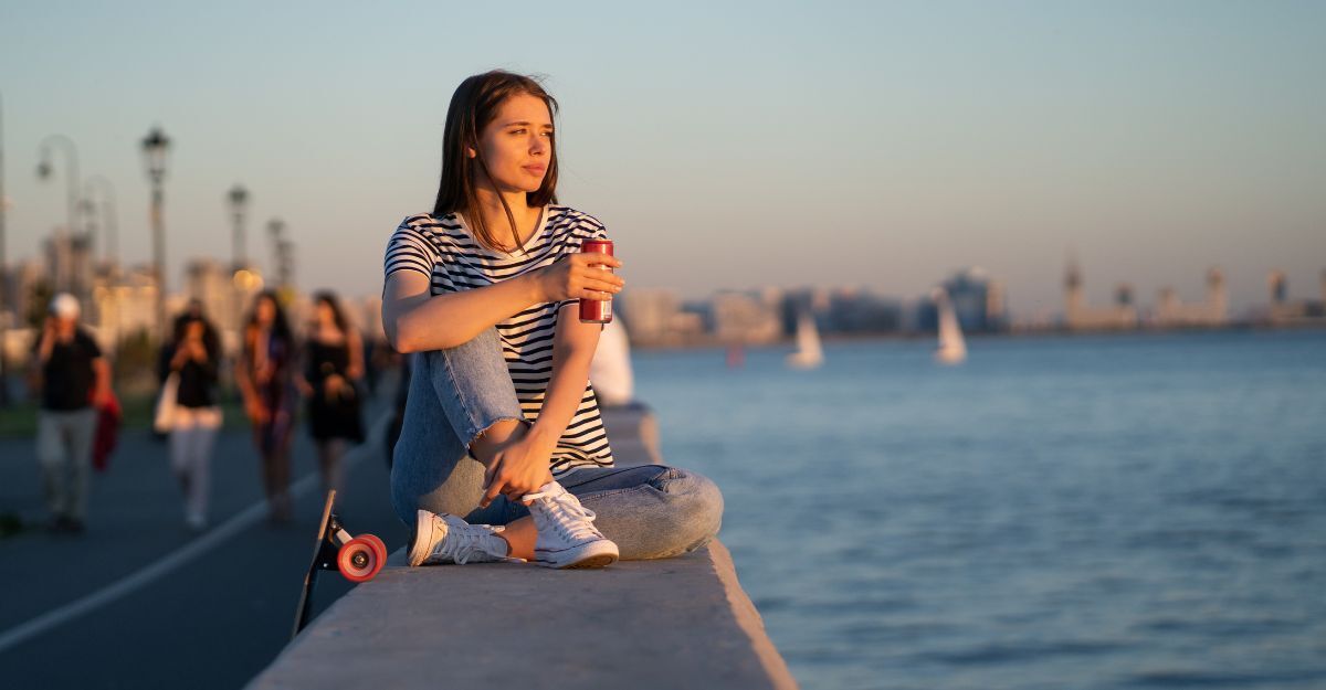 Ragazza osserva il lungomare seduta su un muretto con aria malinconica