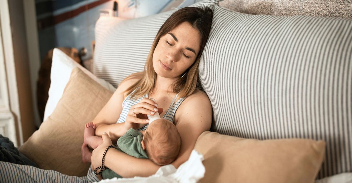 Ragazza sdraiata sul letto con neonato mentre dà il biberon