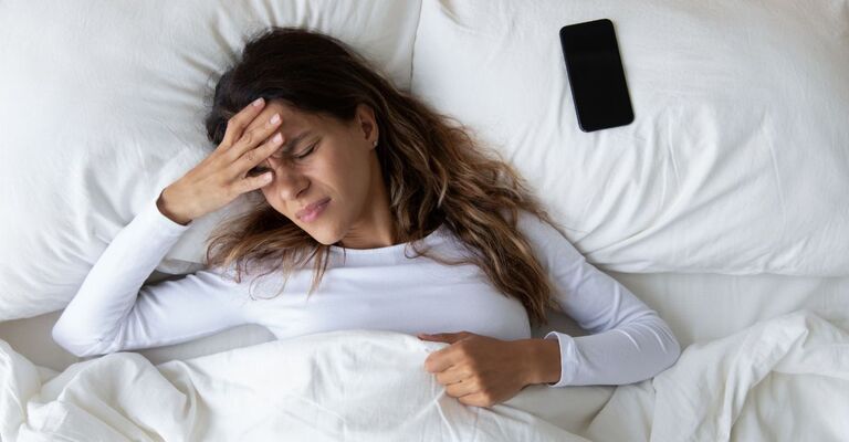 Donna sdraiata al letto col telefono vicino