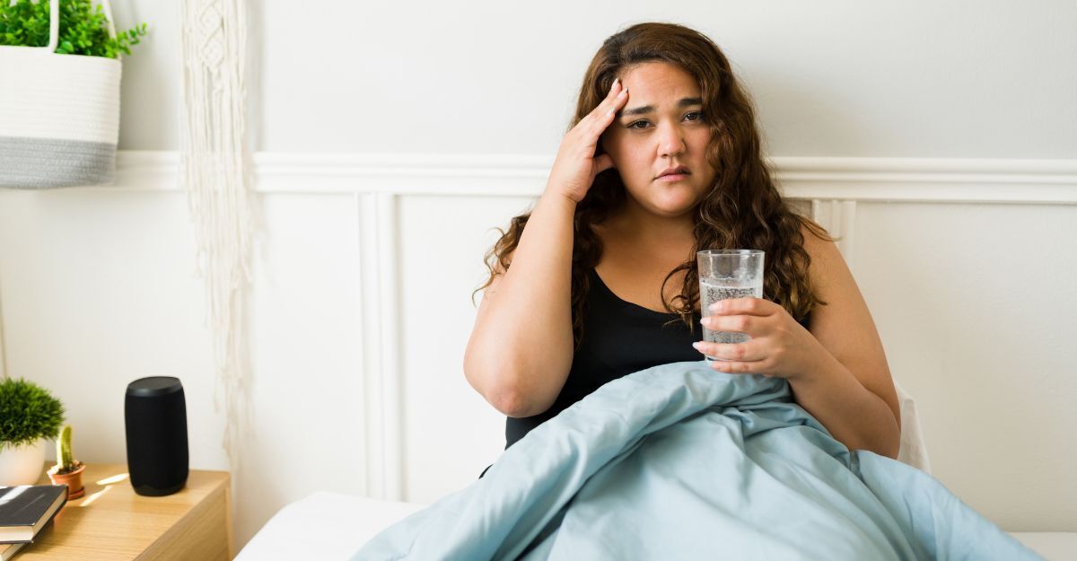 Ragazza nel letto con il mal di testa e un bicchiere d'acqua in mano
