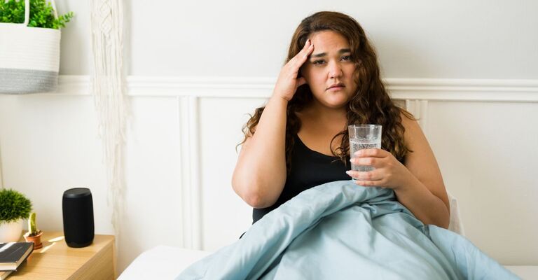 Ragazza nel letto con il mal di testa e un bicchiere d'acqua in mano