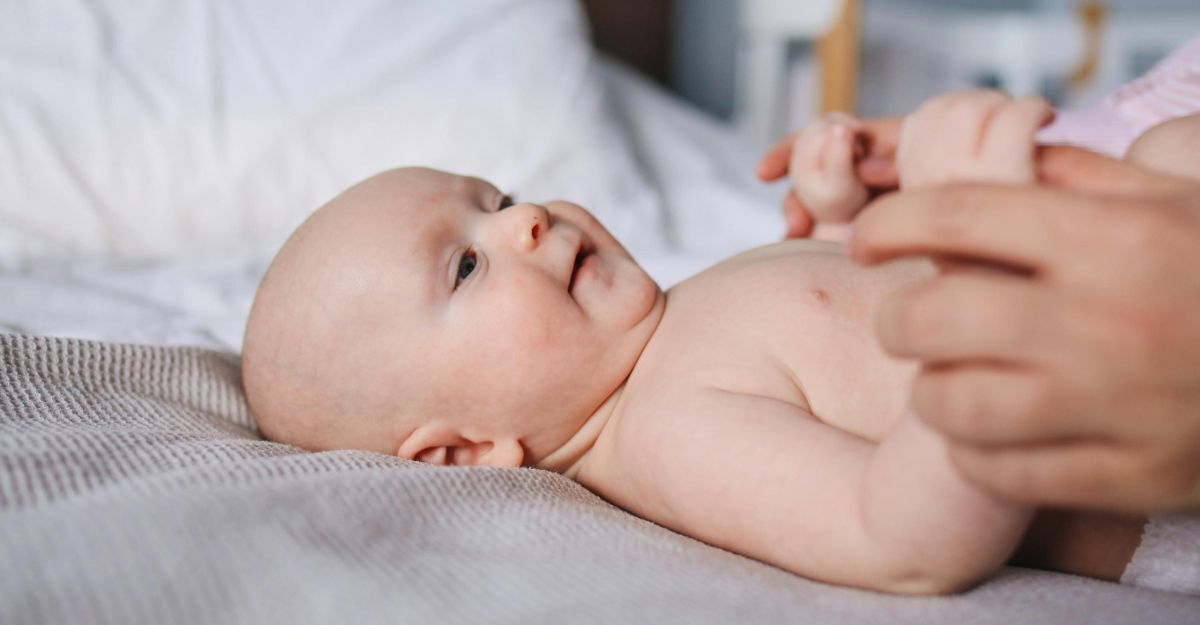 Neonato sdraiato con una persona che gli tiene le mani e ci gioca