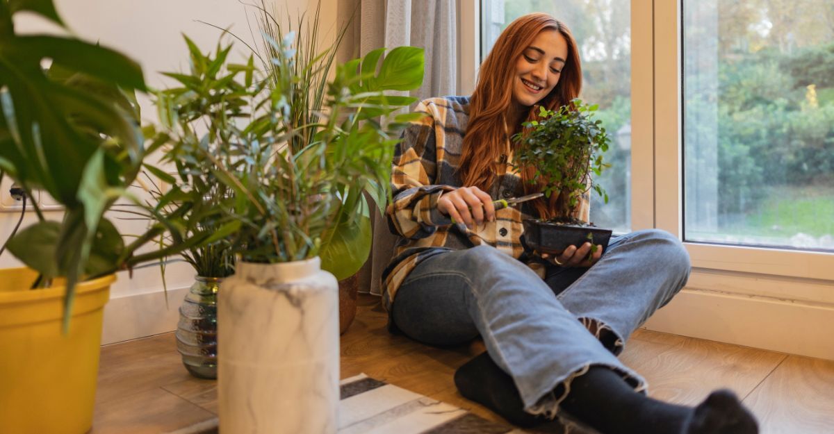 Ragazza seduta sul pavimento del suo appartamento che cura il suo bonsai circondata da piante