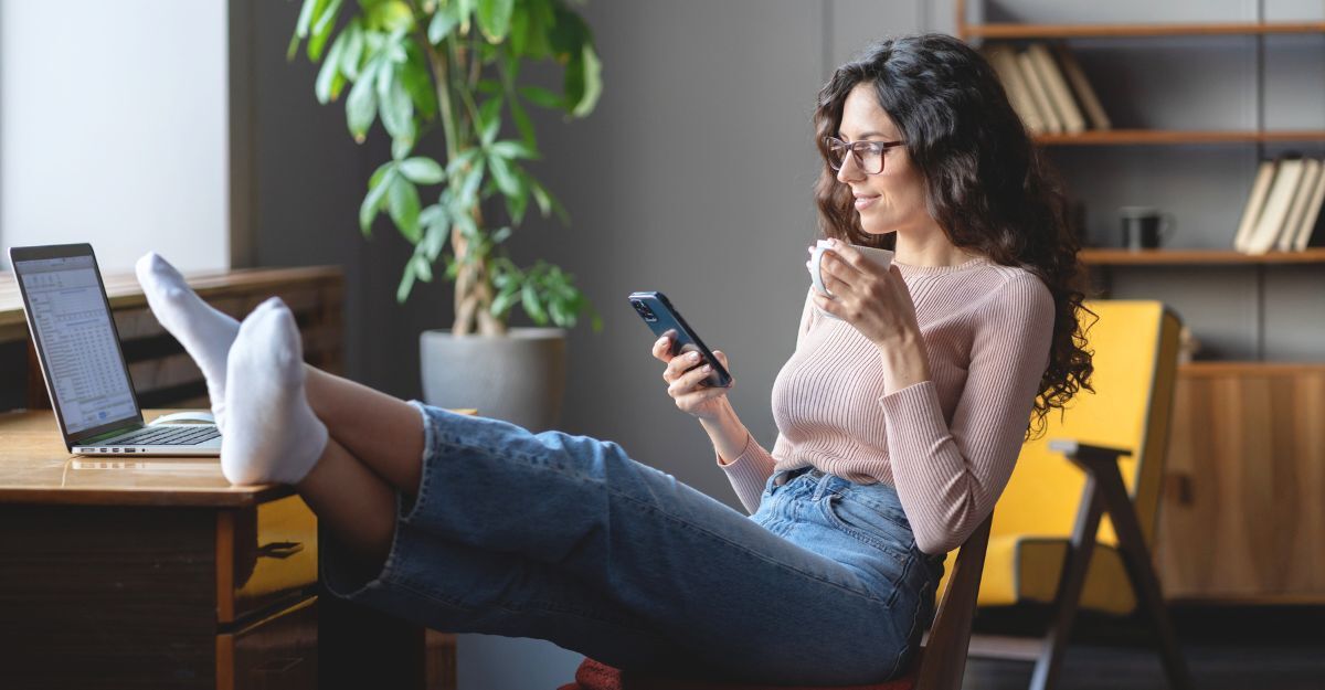 Ragazza che scrolla sul telefono mentre è seduta con le gambe sul tavolo