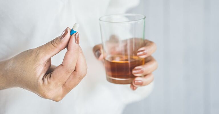 Donna con pillola in una mano e bicchiere di alcol nell'altra