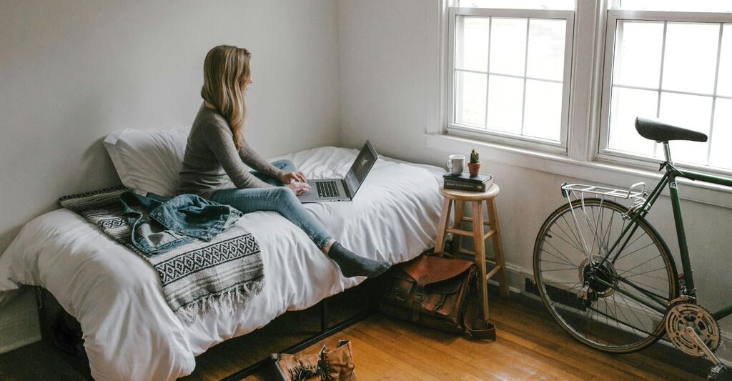Ragazza in camera con bicicletta che legge articoli sul suo PC seduta su letto