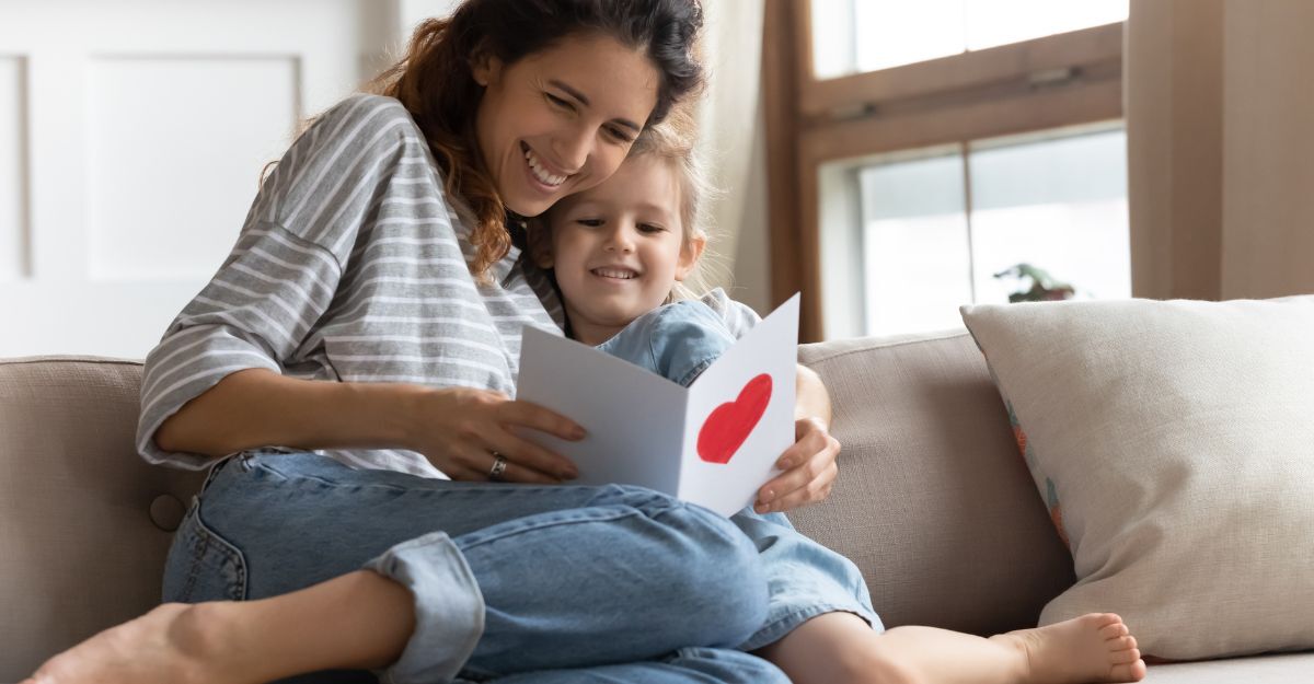 mamma e figlia si abbracciano sul divano mentre leggono un biglietto di auguri
