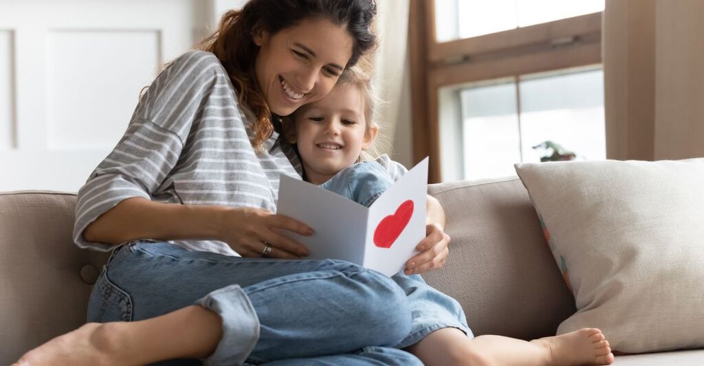 mamma e figlia si abbracciano sul divano mentre leggono un biglietto di auguri