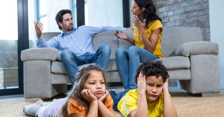 famiglia in casa, genitori sul divano litigano, bambini in primo piano guardano la tv